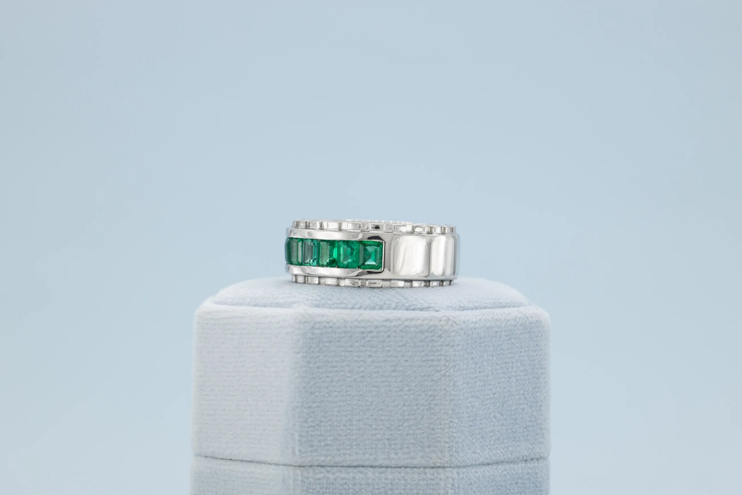Silver ring with green gemstones on a light blue background