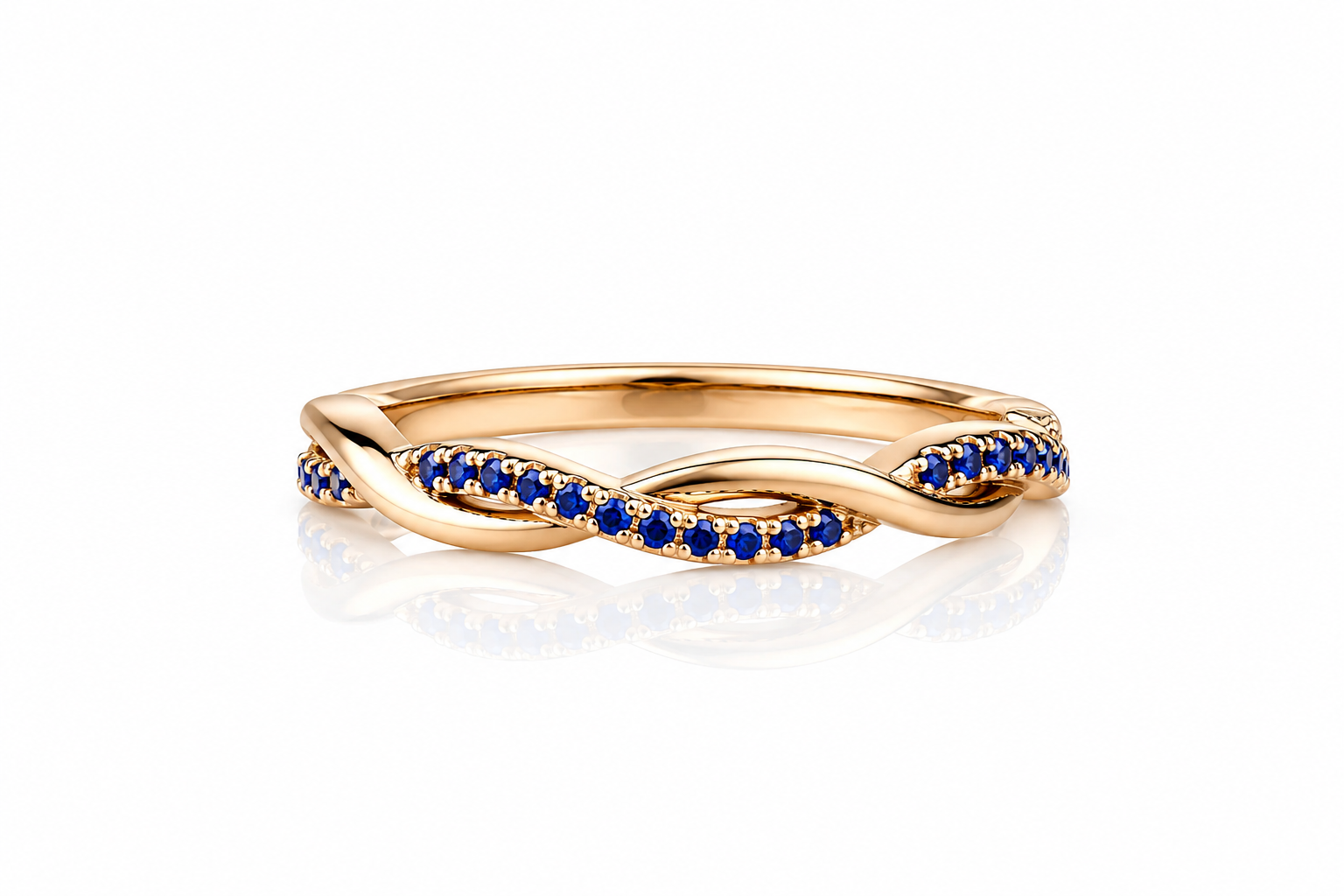 A twisted infinity-style ring in yellow gold, accented with rows of small round-cut deep blue sapphires on the front, shown on a clean white background with a soft reflection below.